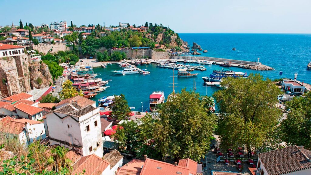 Scenic view of Antalya with turquoise beaches, historic ruins, and lush green cliffs.